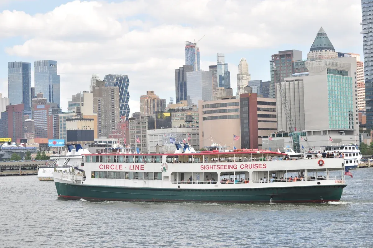A Circle Line sightseeing cruise boat on the Hudson River with the Midtown West skyline behind, seen from a water taxi, part of a New York architecture boat tour