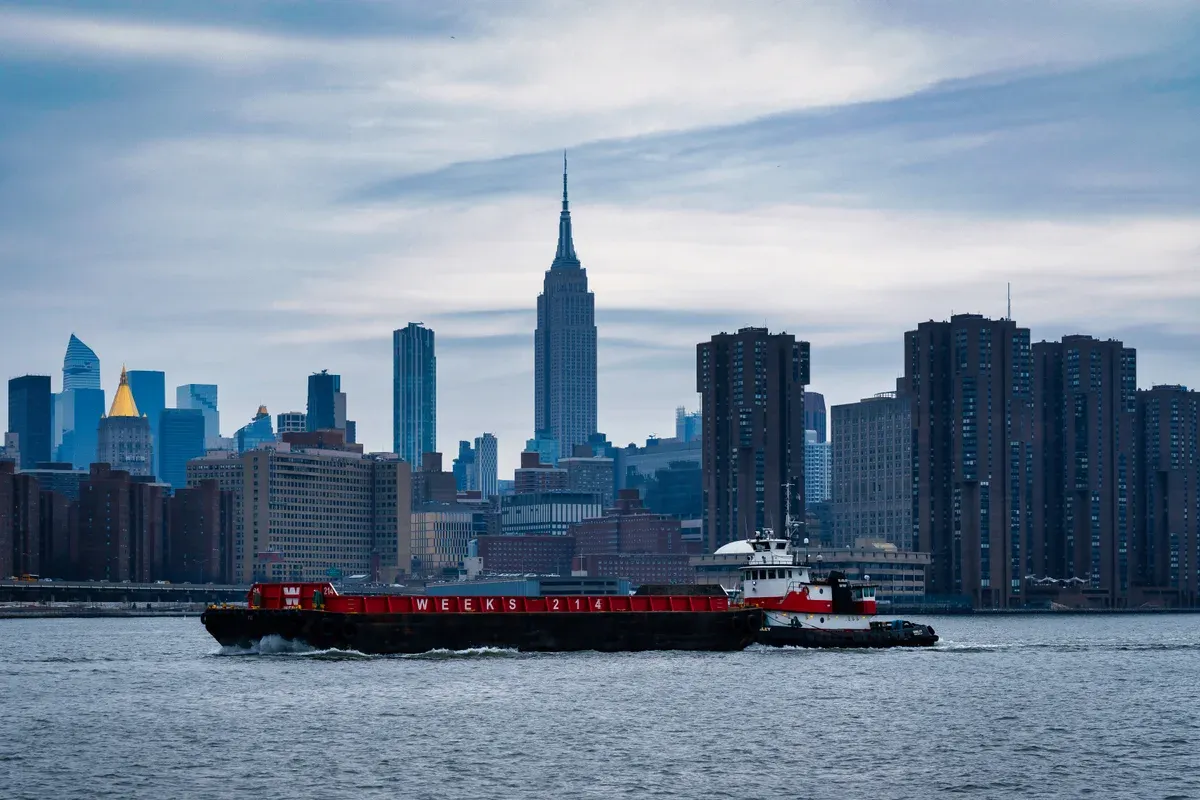 The Midtown Manhattan skyline with the Empire State Building, seen across the East River from Long Island City with a tug and barge in the foreground, seen on a New York architecture boat tour